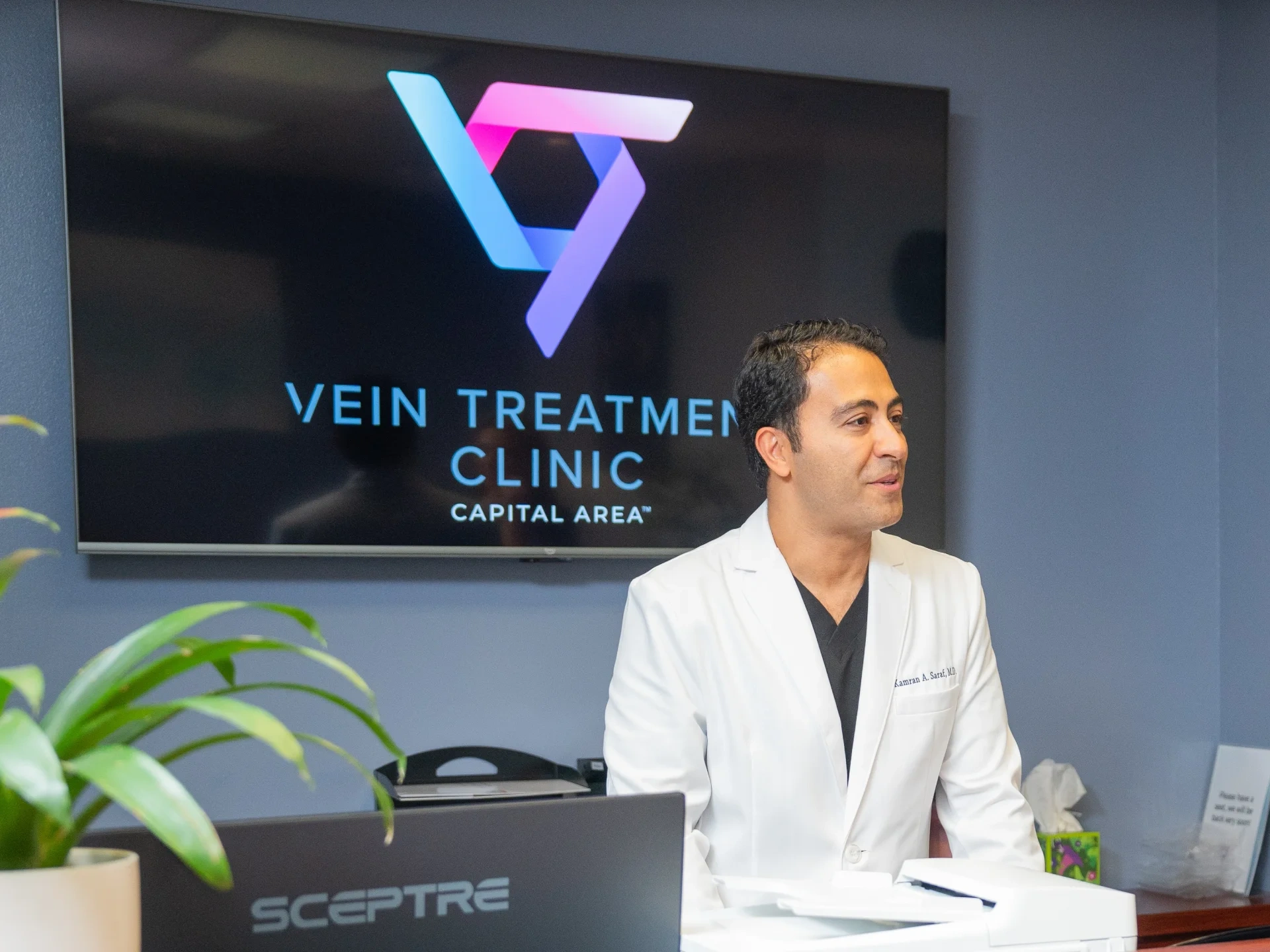 Dr. Kamran Saraf stands behind the reception desk at a Vein Treatment Clinic